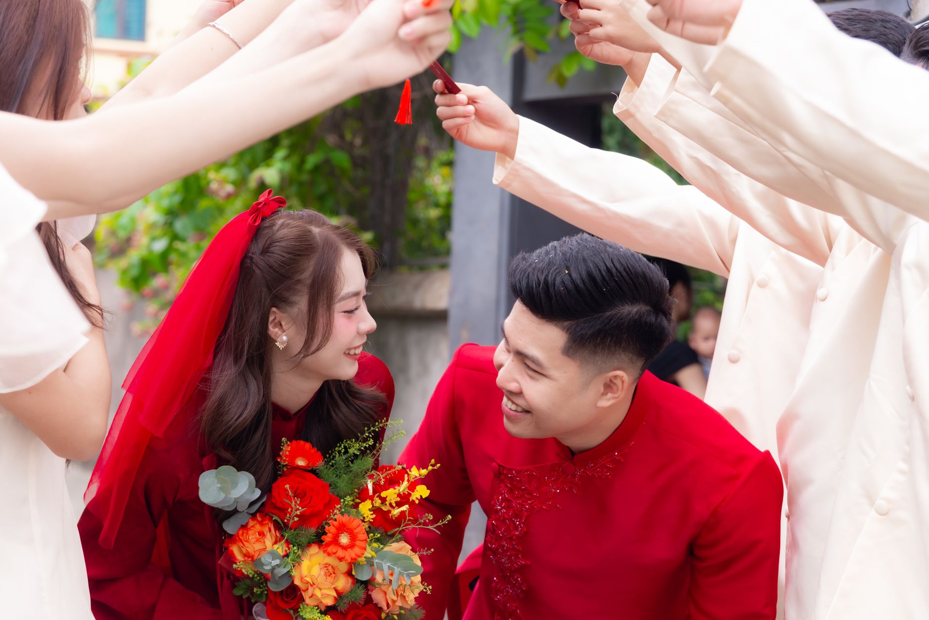 A vibrant Asian couple celebrates their wedding surrounded by friends outdoors, adorned in traditional attire.