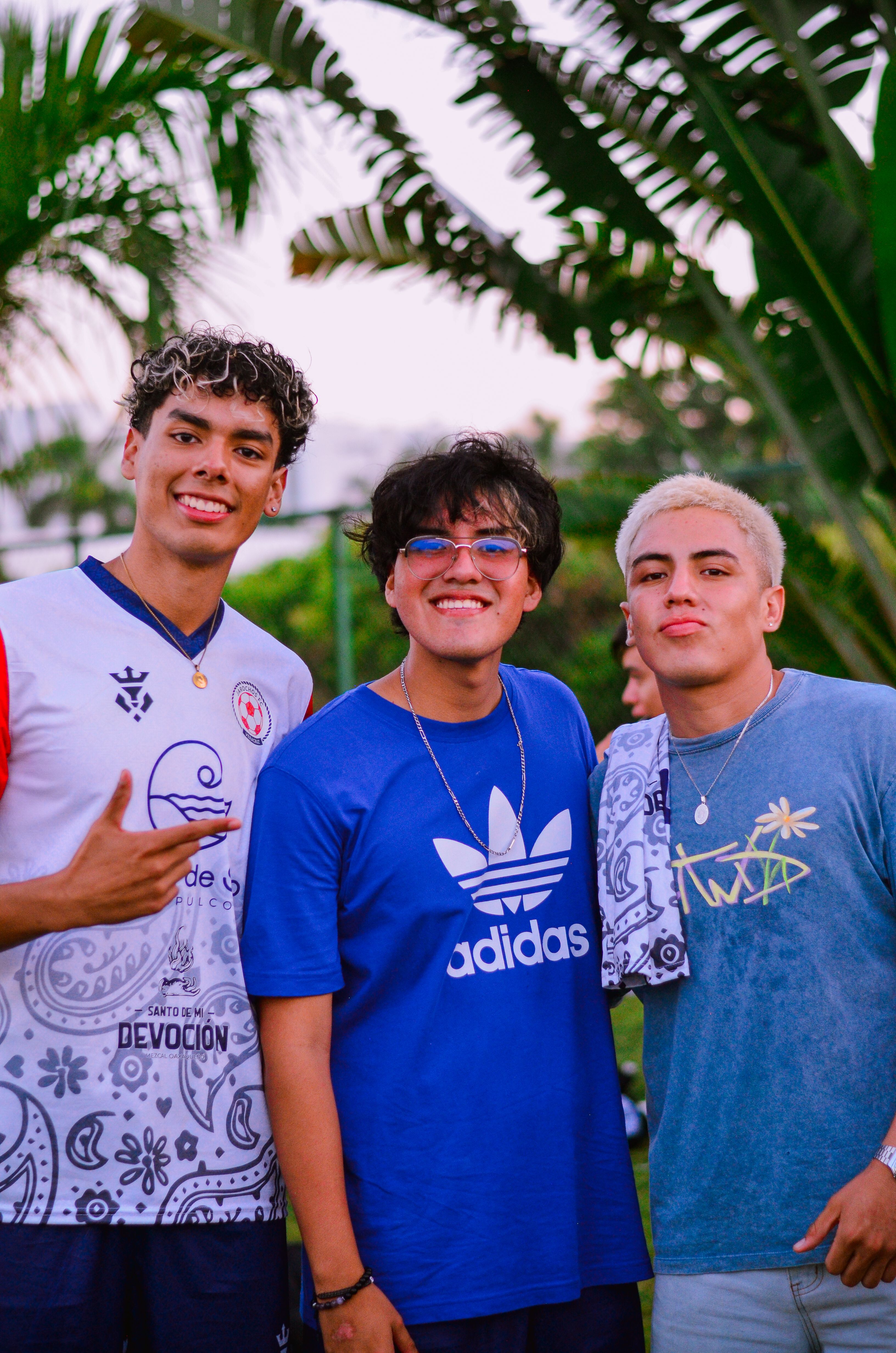 Three Friends Posing Outdoors with Tropical Background · Free Stock Photo