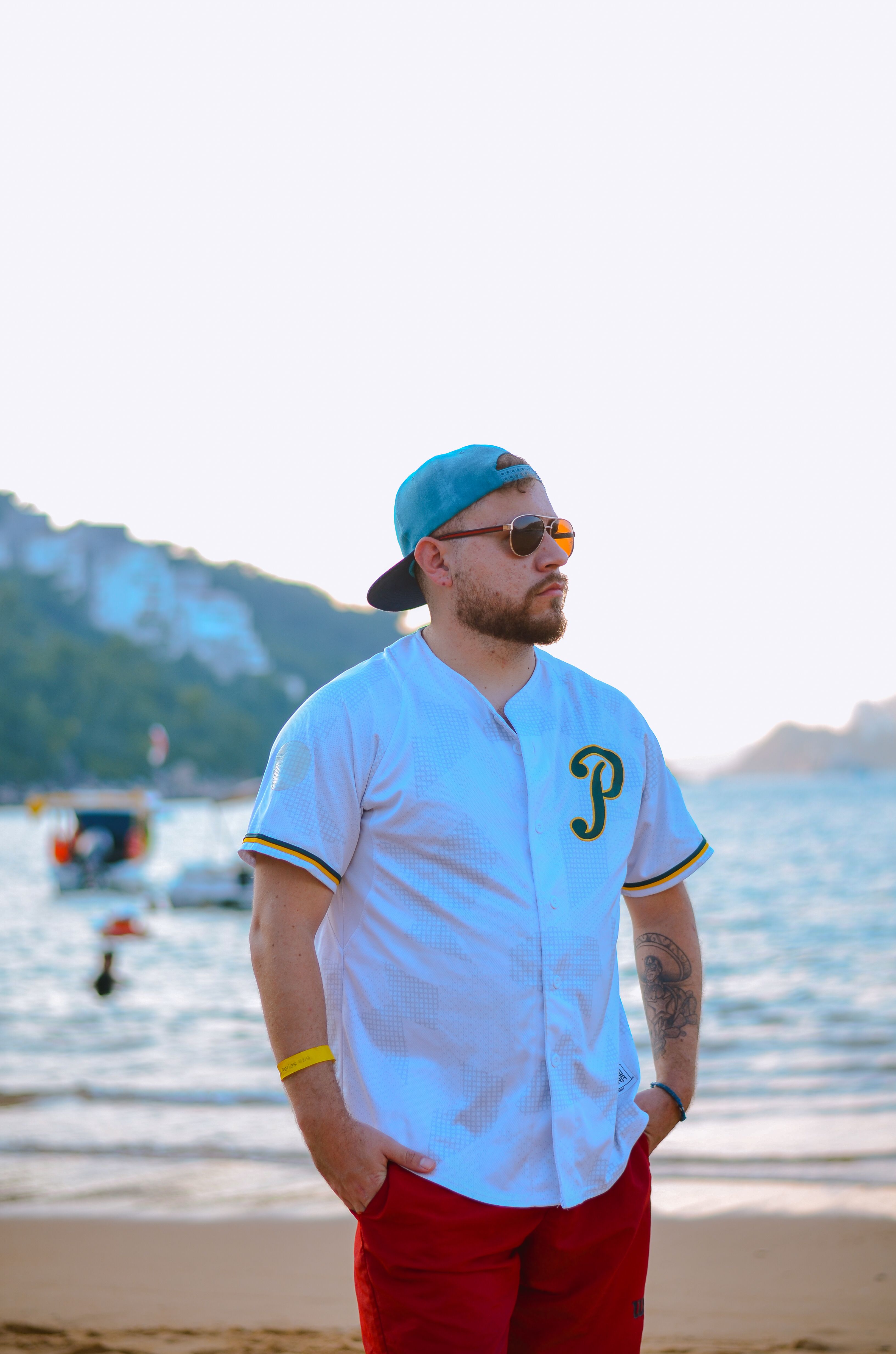 Casual man in baseball jersey standing on beach at sunset, enjoying the view.