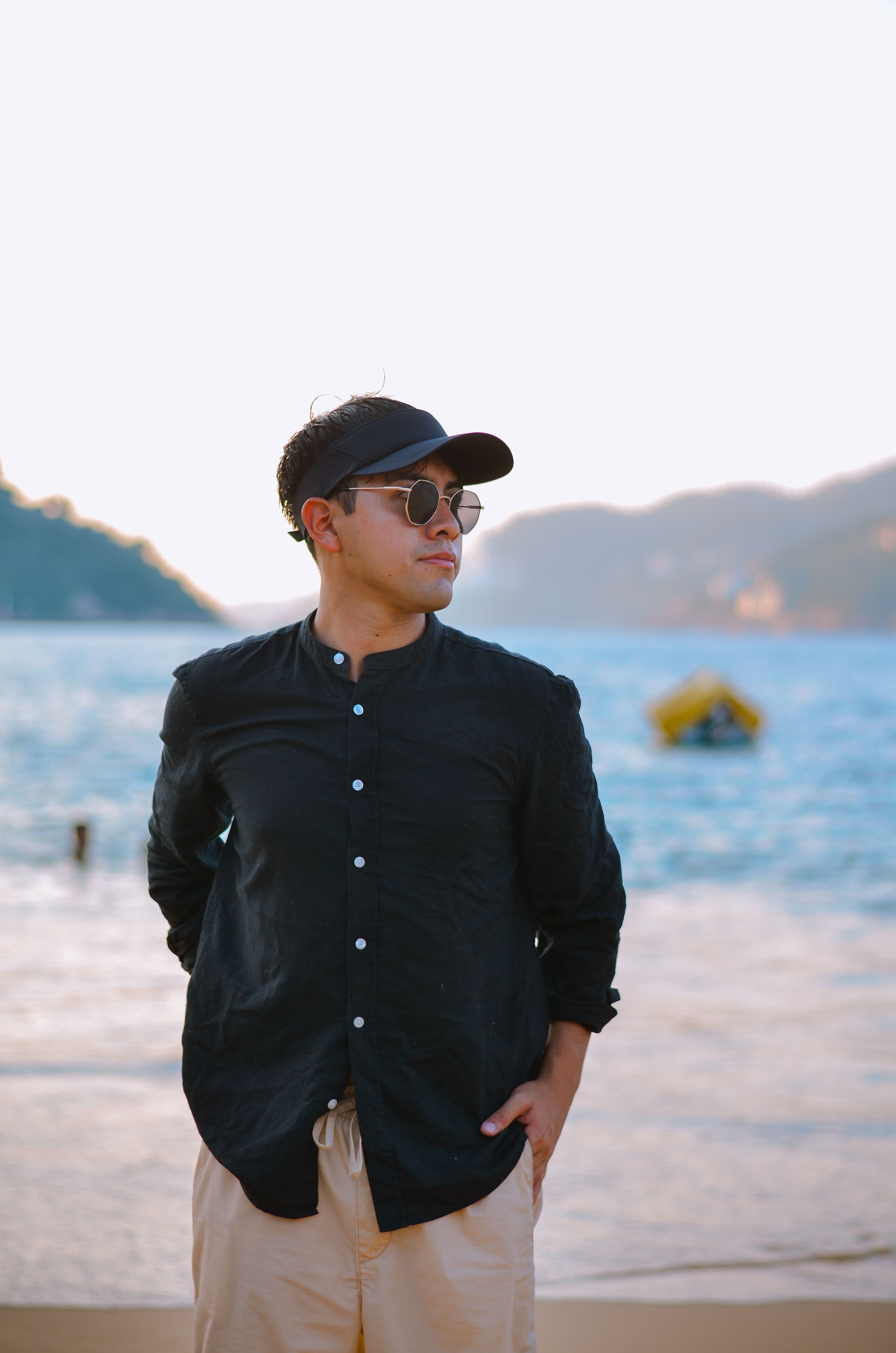 Stylish man posing on beach at sunset in summer holiday outfit