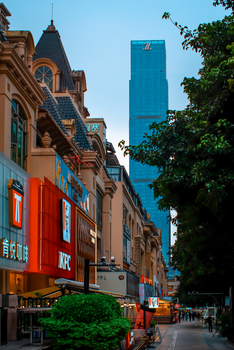 Vibrant city street view with tall skyscraper and lively storefronts at dusk.