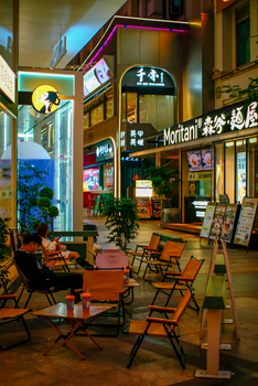 Outdoor cafe scene at night with neon lights and glowing signage.