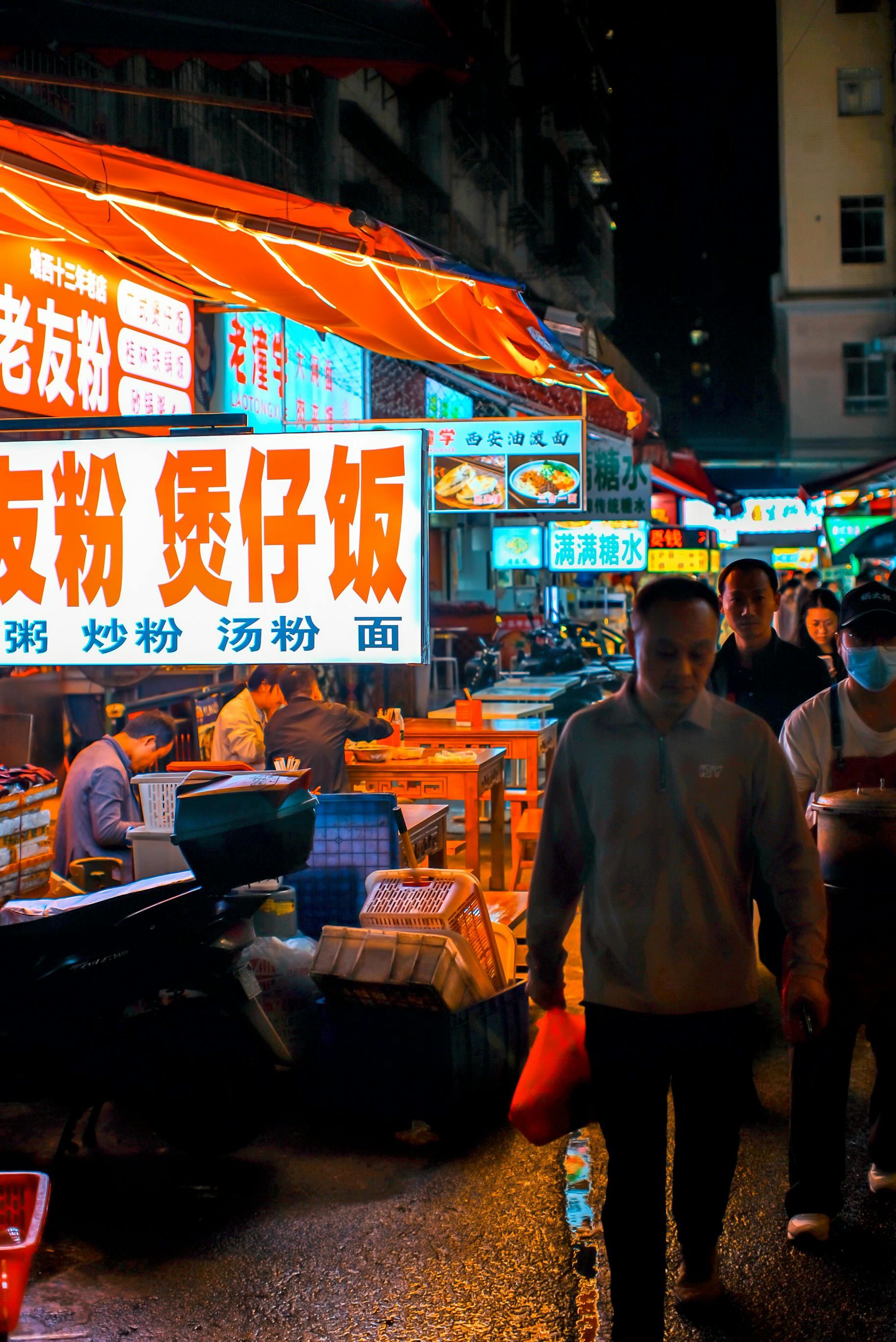 A lively night scene at an Asian street market with neon signs and bustling pedestrians.