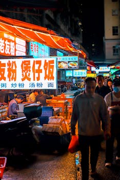 A lively night scene at an Asian street market with neon signs and bustling pedestrians.
