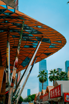 Modern architectural structure with skyscrapers and palm trees under blue sky.