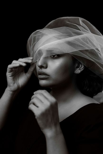 Elegant black and white portrait of a woman partially covered by a veil, showcasing style and mystery.