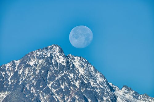 Free A breathtaking view of the moon rising above snow-capped mountains in the High Tatras, Slovakia. Stock Photo