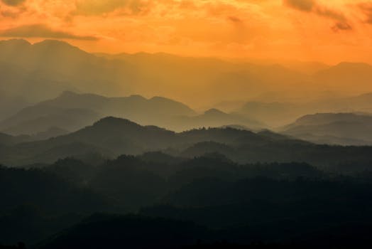 Captivating view of layered mountain ranges under a fiery sunset sky, creating a calm and serene atmosphere.