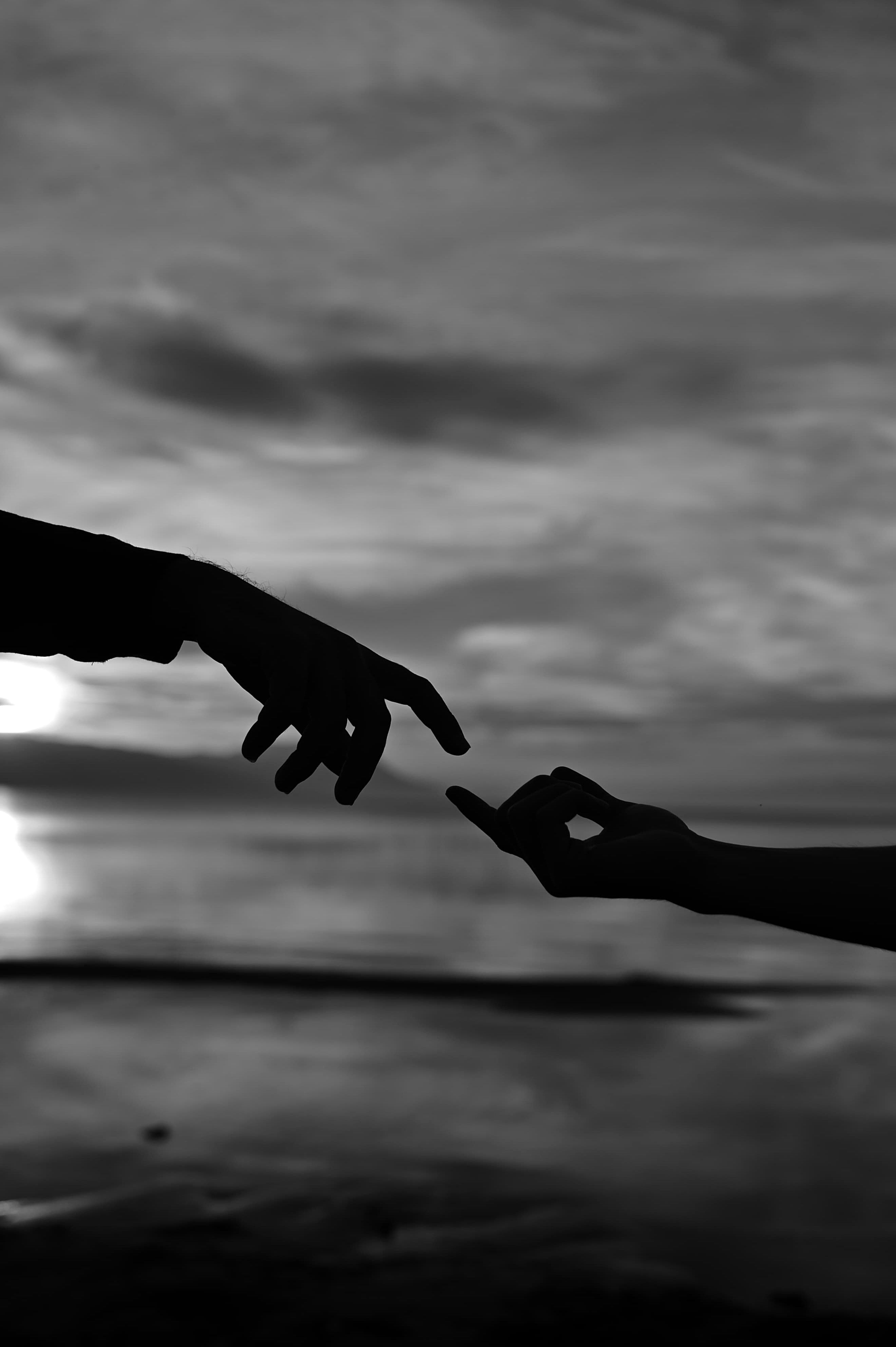 Fotomural Silueta artística en blanco y negro de dos manos extendidas que se tocan al atardecer.