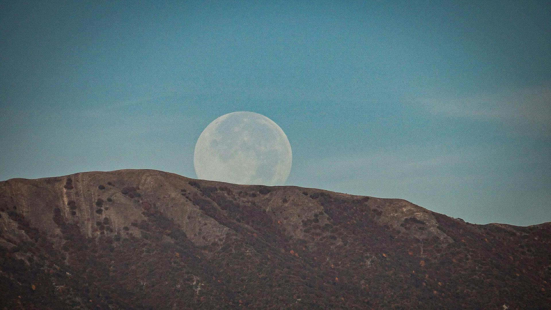 Majestic view of the moon rising above a rugged mountain range under clear sky.