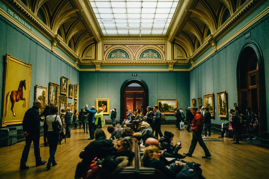 Visitors gathered in a grand gallery hall looking at paintings