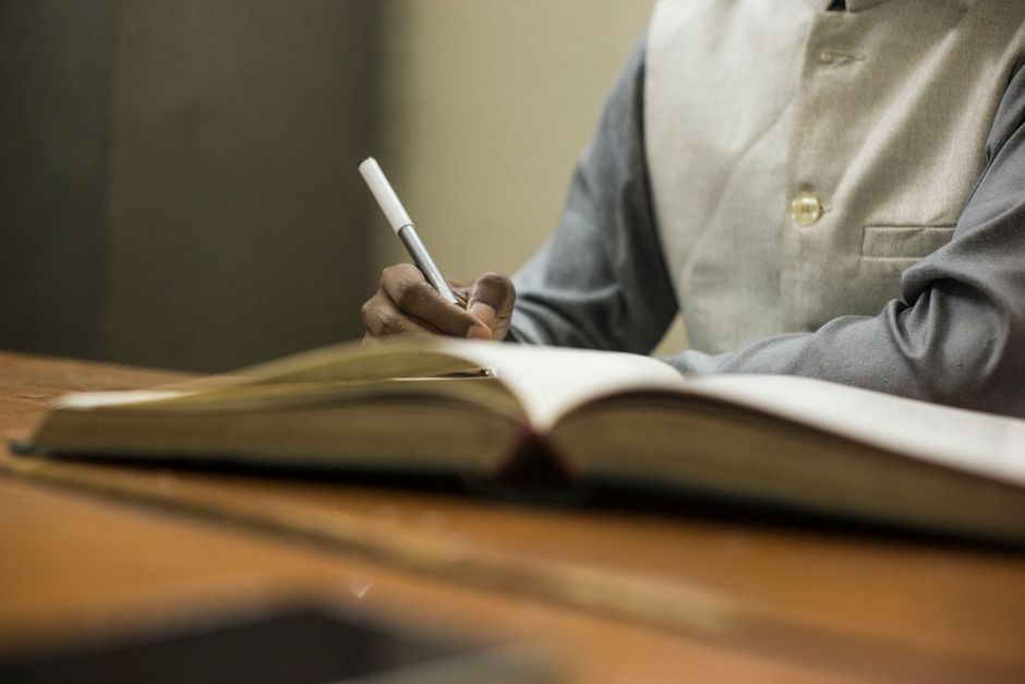 What should you check for citations in custom assignment writing services? 2 A person in a formal setting writes in a notebook at a wooden desk.
