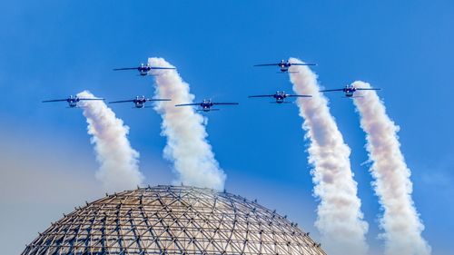 Free Jets in formation releasing smoke trails fly over a geodesic dome under clear blue skies. Stock Photo