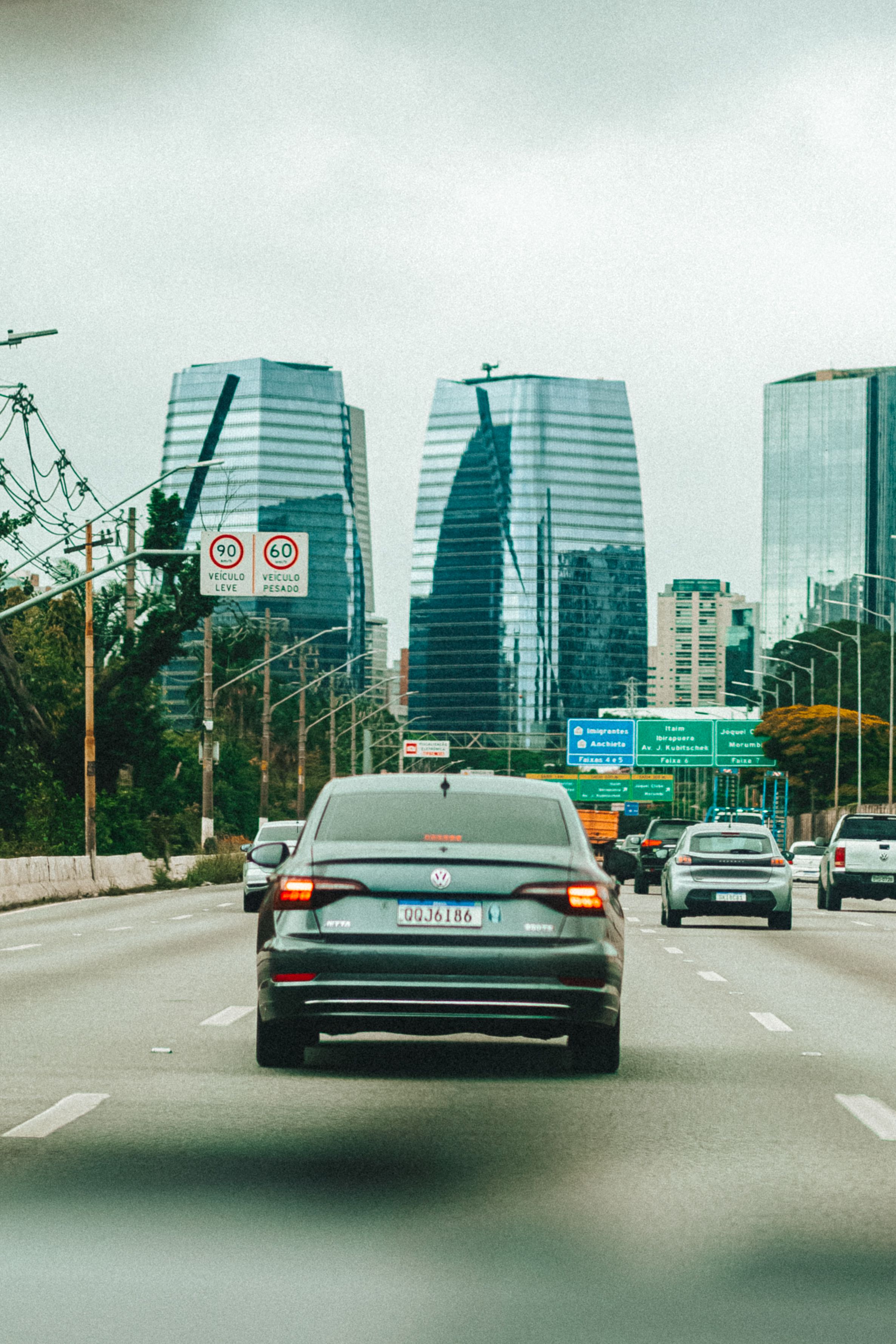 Fotomural Coches circulando por una autopista concurrida con modernos rascacielos a lo lejos, mostrando la vida urbana.