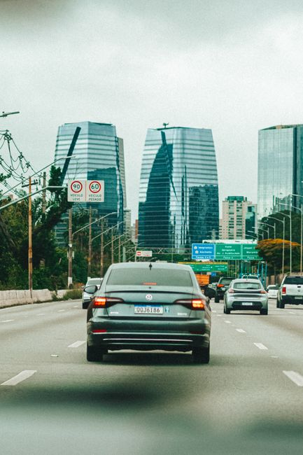 Fotomural Coches circulando por una autopista concurrida con modernos rascacielos a lo lejos, mostrando la vida urbana.