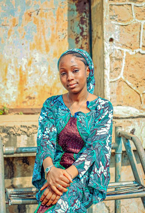 Free A woman in traditional attire sits on a bench outdoors, radiating confidence and elegance. Stock Photo