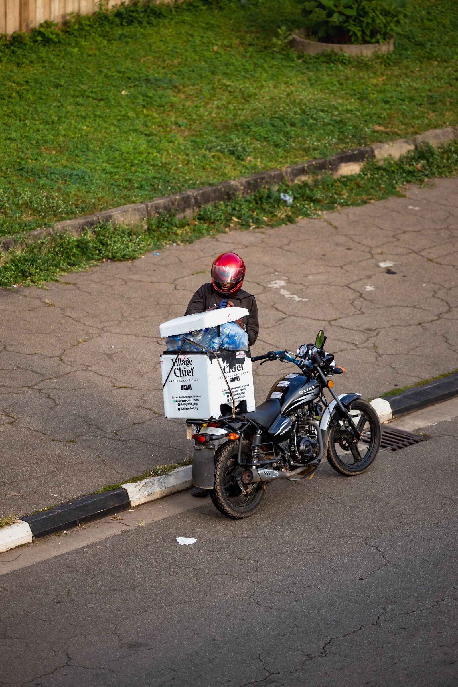 Livreur à moto casqué avec sa caisse de livraison dans une rue