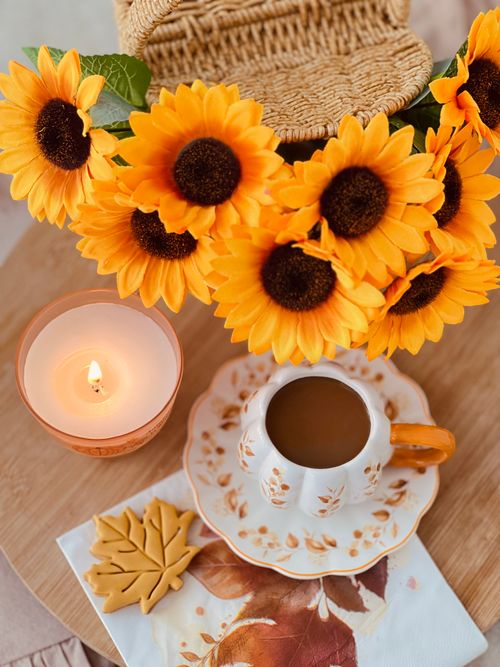 Free A cozy autumn scene featuring a coffee cup, bright sunflowers, and a lit candle on a wooden table. Stock Photo