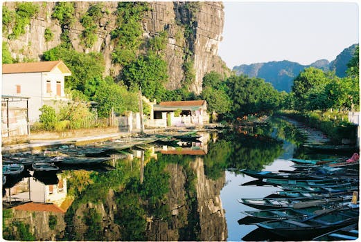 Peaceful river scene with boats, limestone cliffs, and green reflections in Hoa Lư, Vietnam.