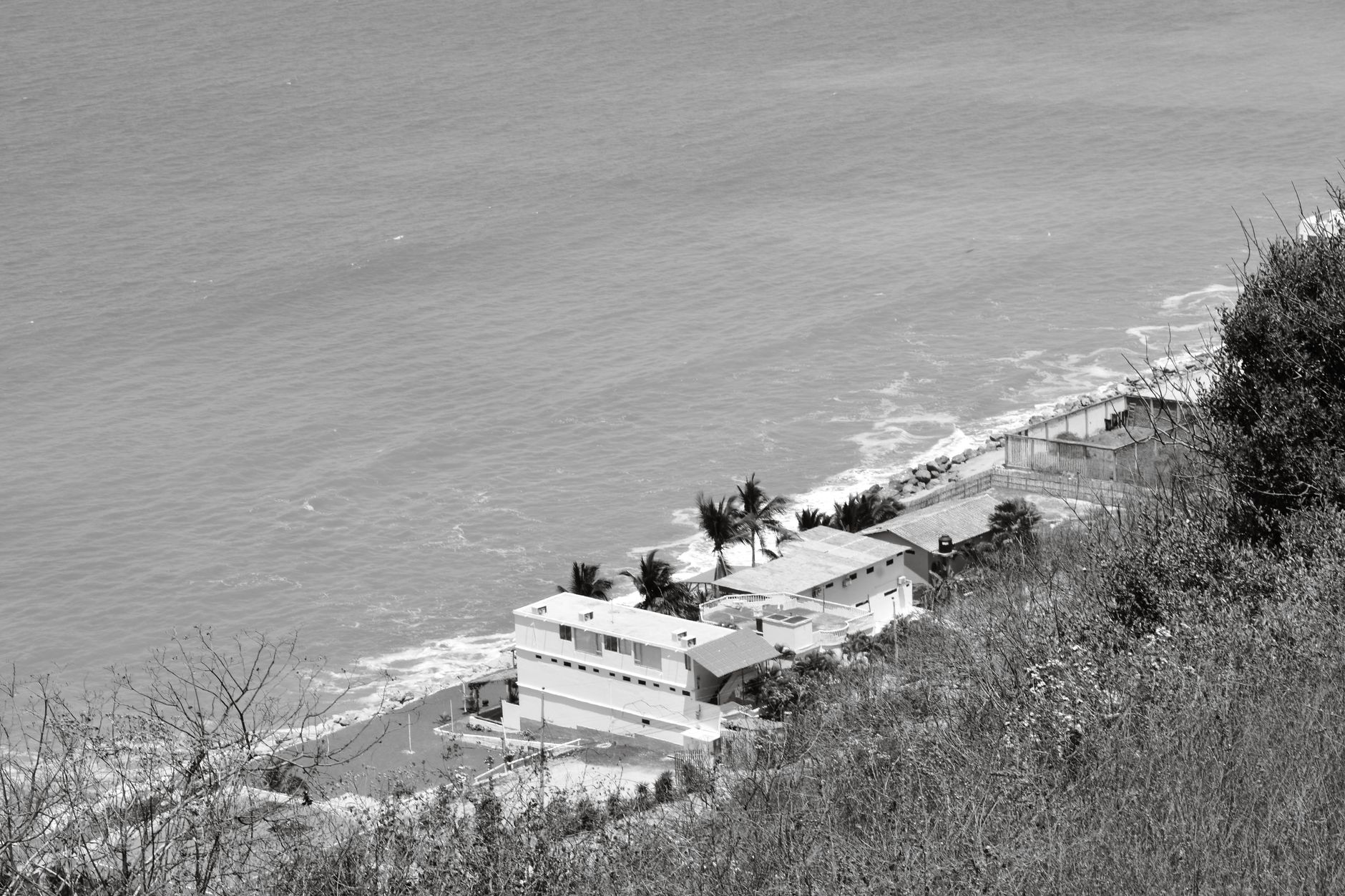 Aerial view of coastal buildings by the ocean in Ecuador, captured in black and white.