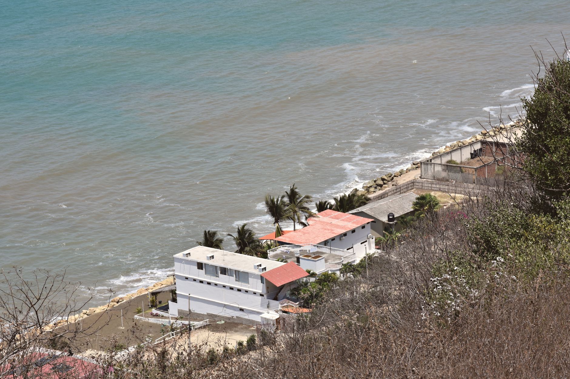 Aerial view of coastal homes along the shoreline in Ecuador, featuring clear ocean waters and lush greenery.