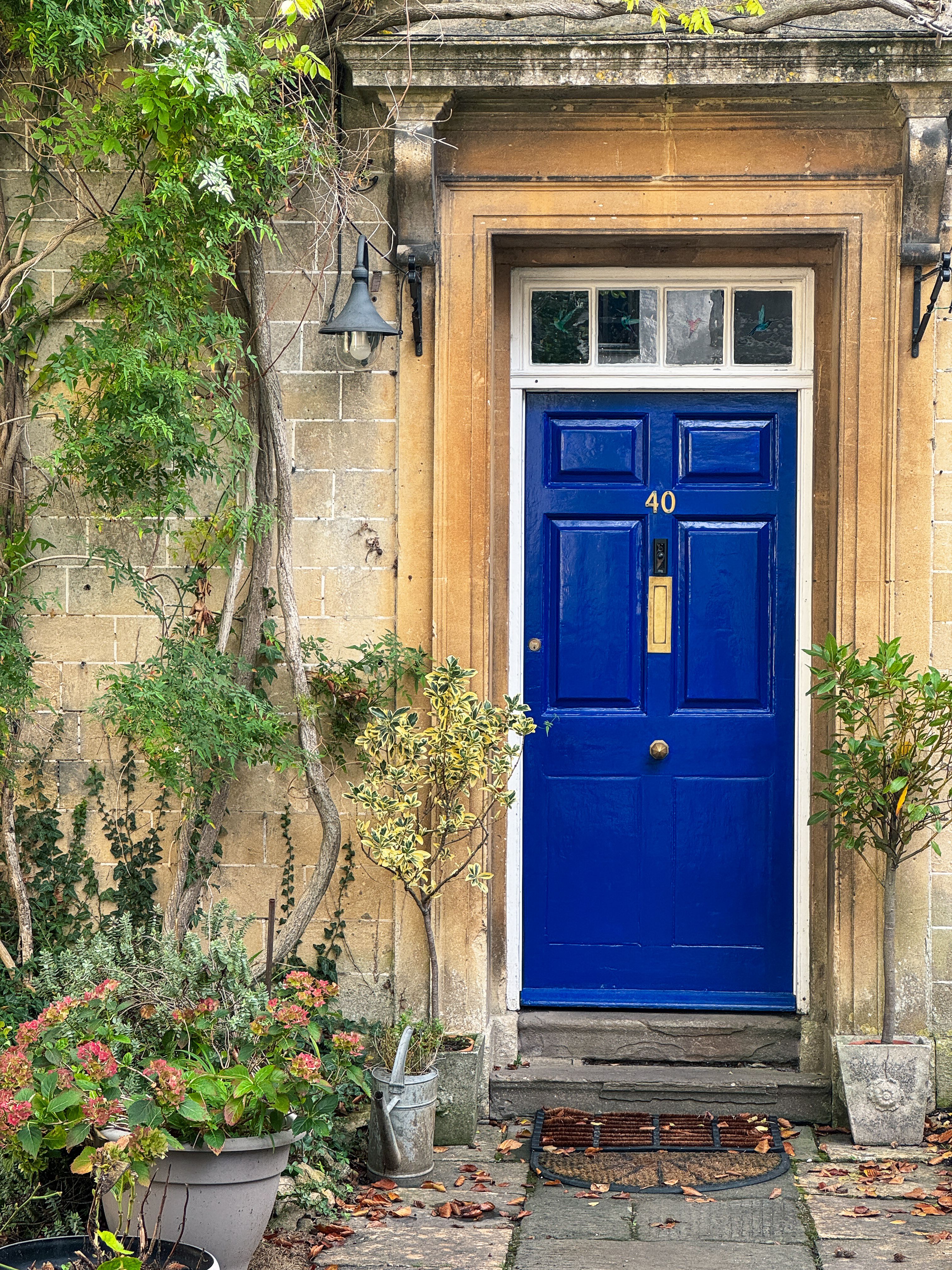 A vibrant blue door in a classic stone building entrance, surrounded by lush greenery in Corsham, England.