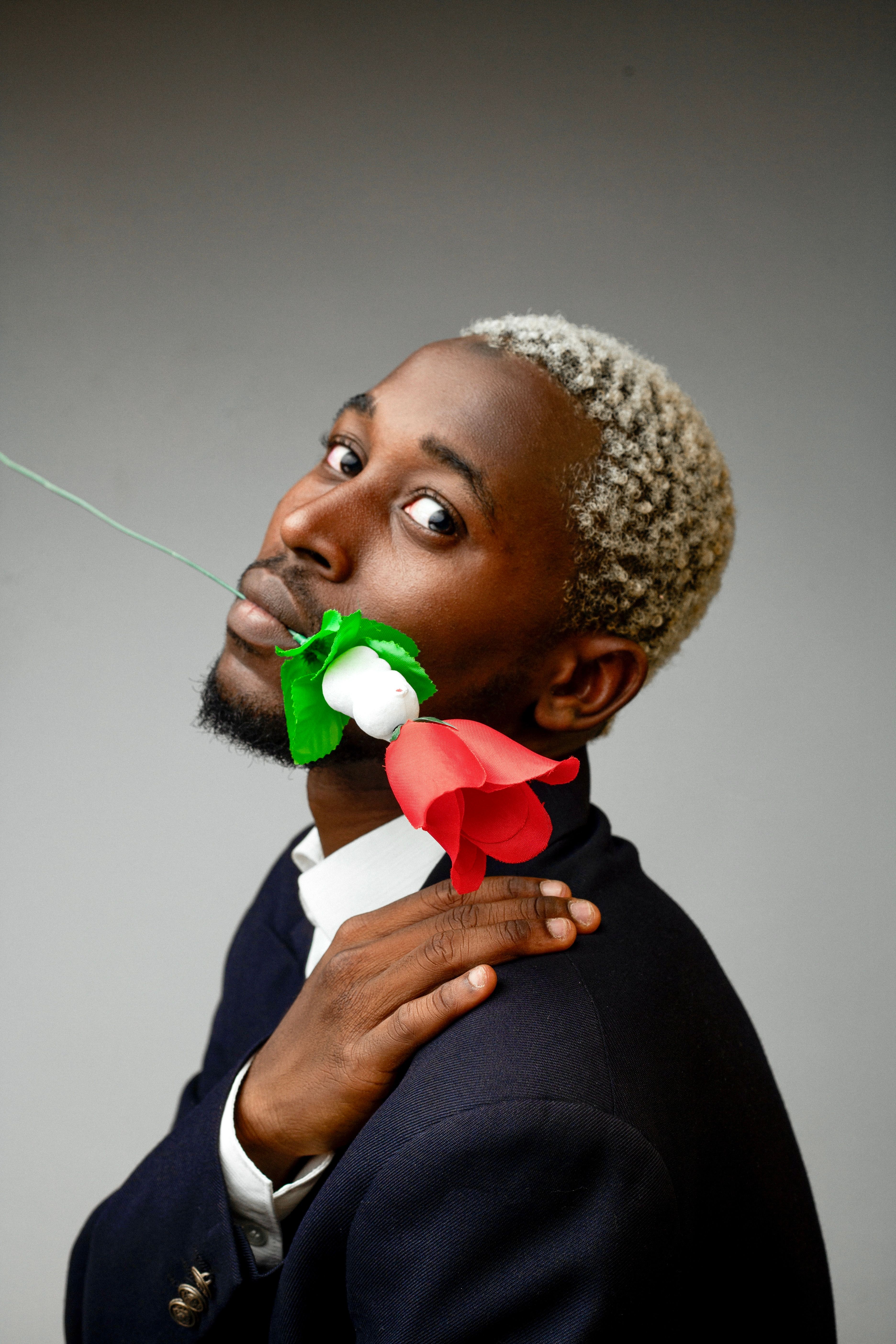 Stylish portrait of a man holding vibrant paper flower, blending art and fashion.