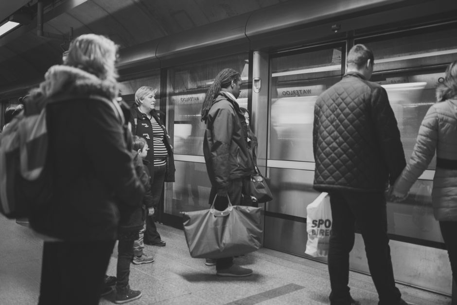 Black and white photo of diverse commuters waiting at a subway station platform.
