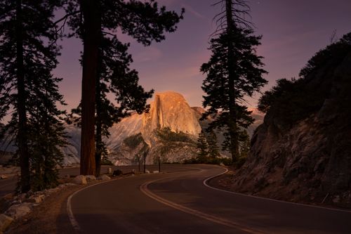 Free Stunning twilight view of Half Dome in Yosemite National Park with winding road and tall trees. Stock Photo