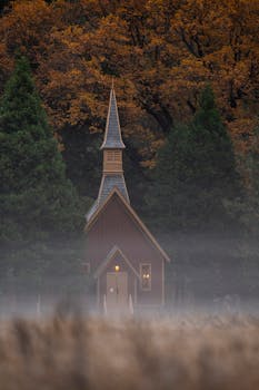 Idyllic chapel surrounded by autumn trees and mist, creating a serene atmosphere.