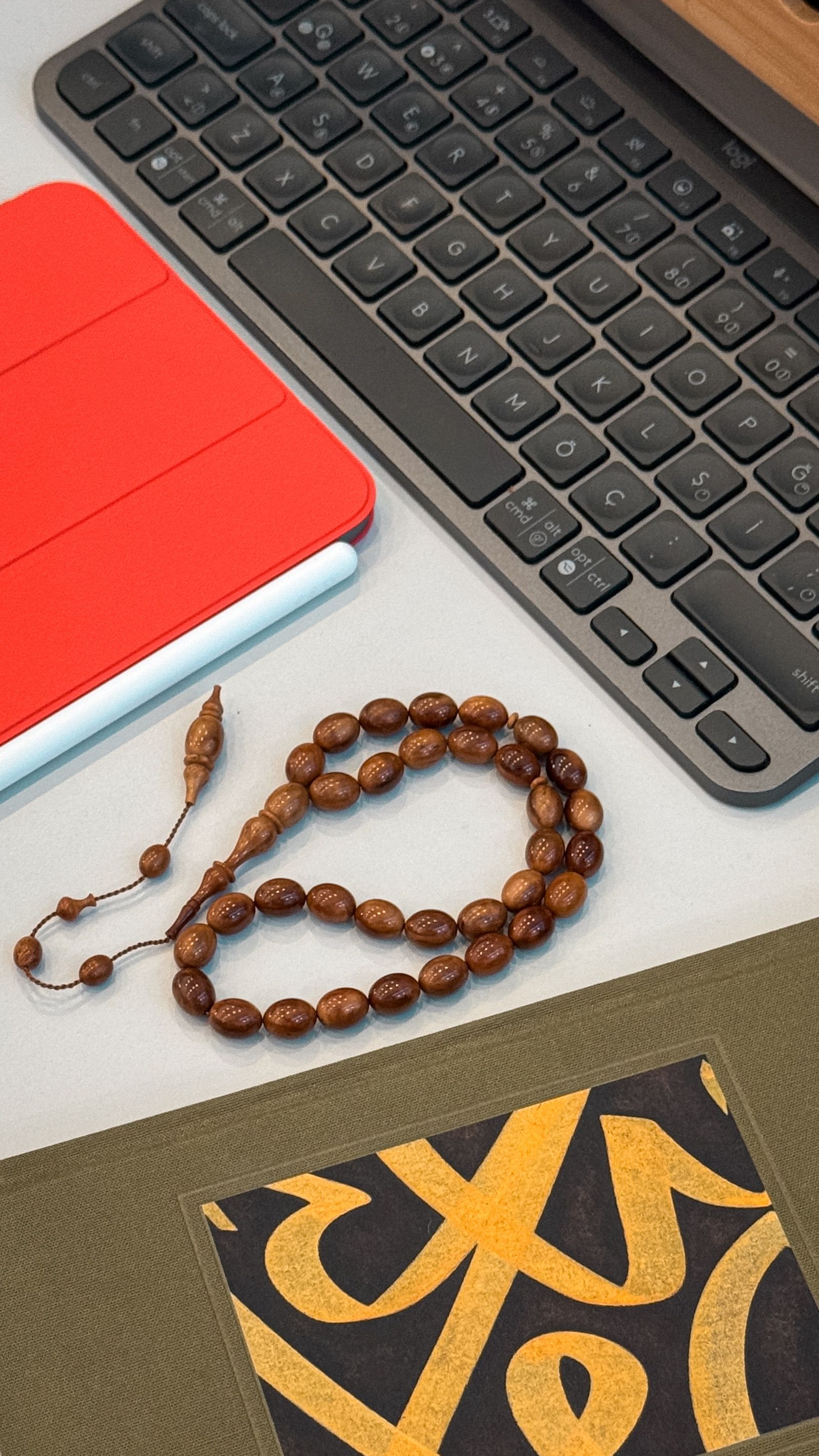 A flat lay of a desk featuring prayer beads, a keyboard, and a red tablet case.