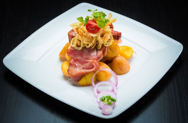 Gourmet dish with bacon, potatoes, and onions on a white plate. Perfect for culinary content.