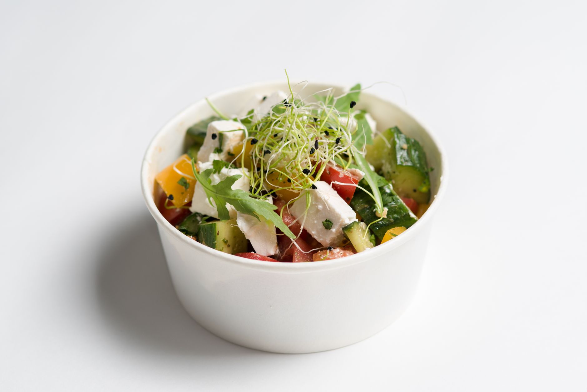 Colorful Mediterranean salad with feta, cucumbers, and sprouts in a white bowl.