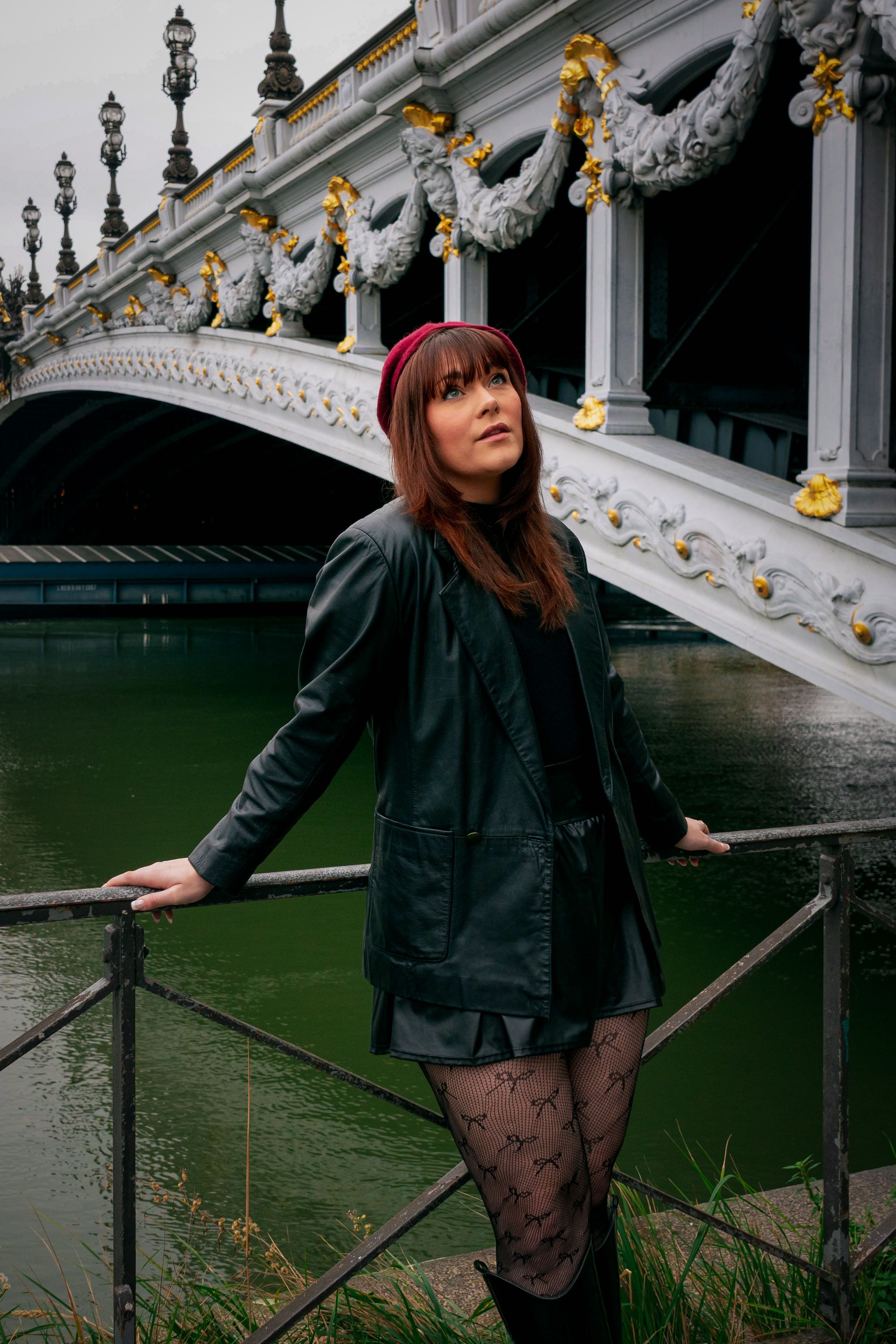 Fashionable woman posing by iconic Paris bridge in autumn attire.
