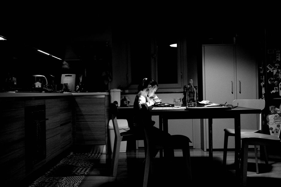 A child studying alone at a dimly lit kitchen table, creating a moody atmosphere.