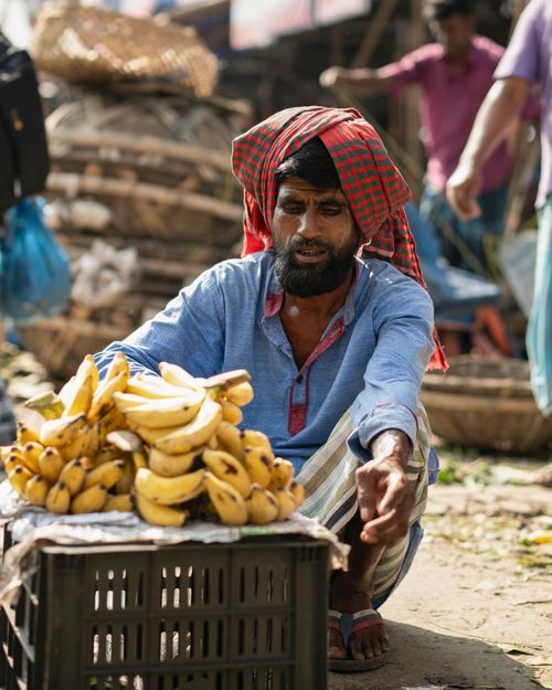 Free A man in Dhaka markets bananas to locals, showcasing vibrant market life. Stock Photo