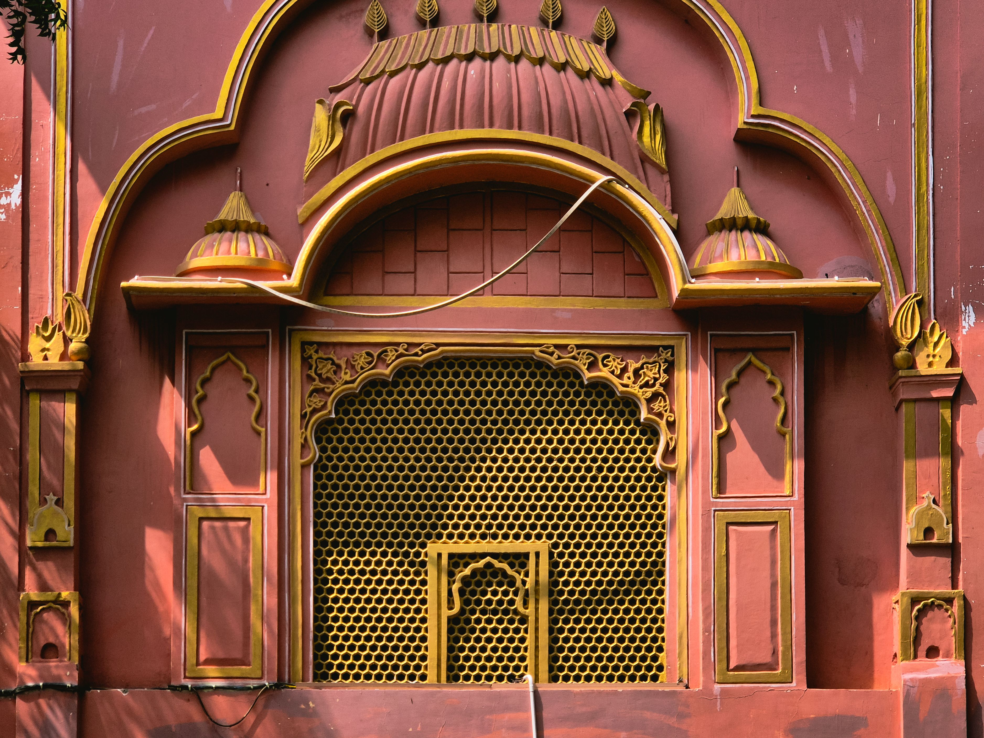 Richly ornate warm-brown building facade in Jaipur with traditional Rajasthani arches, carved detailing and characterful patina
