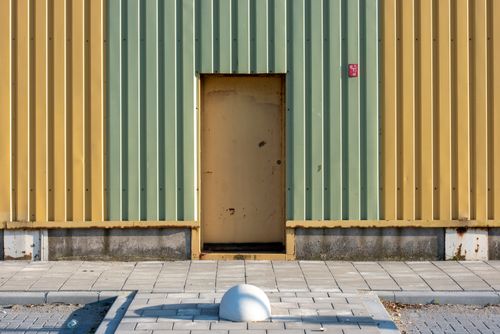 Free Minimalist industrial building facade with yellow and green siding and metal door Stock Photo