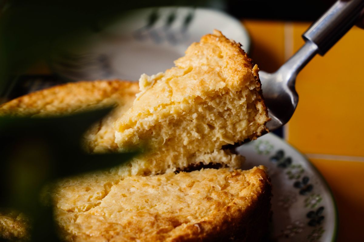 Wedge of moist golden sweet corn bread lifted by a server from a round loaf