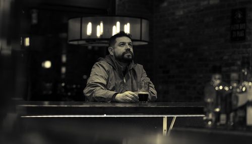 Free Man sitting alone in a dark bar, lost in thought with a drink in hand. Stock Photo