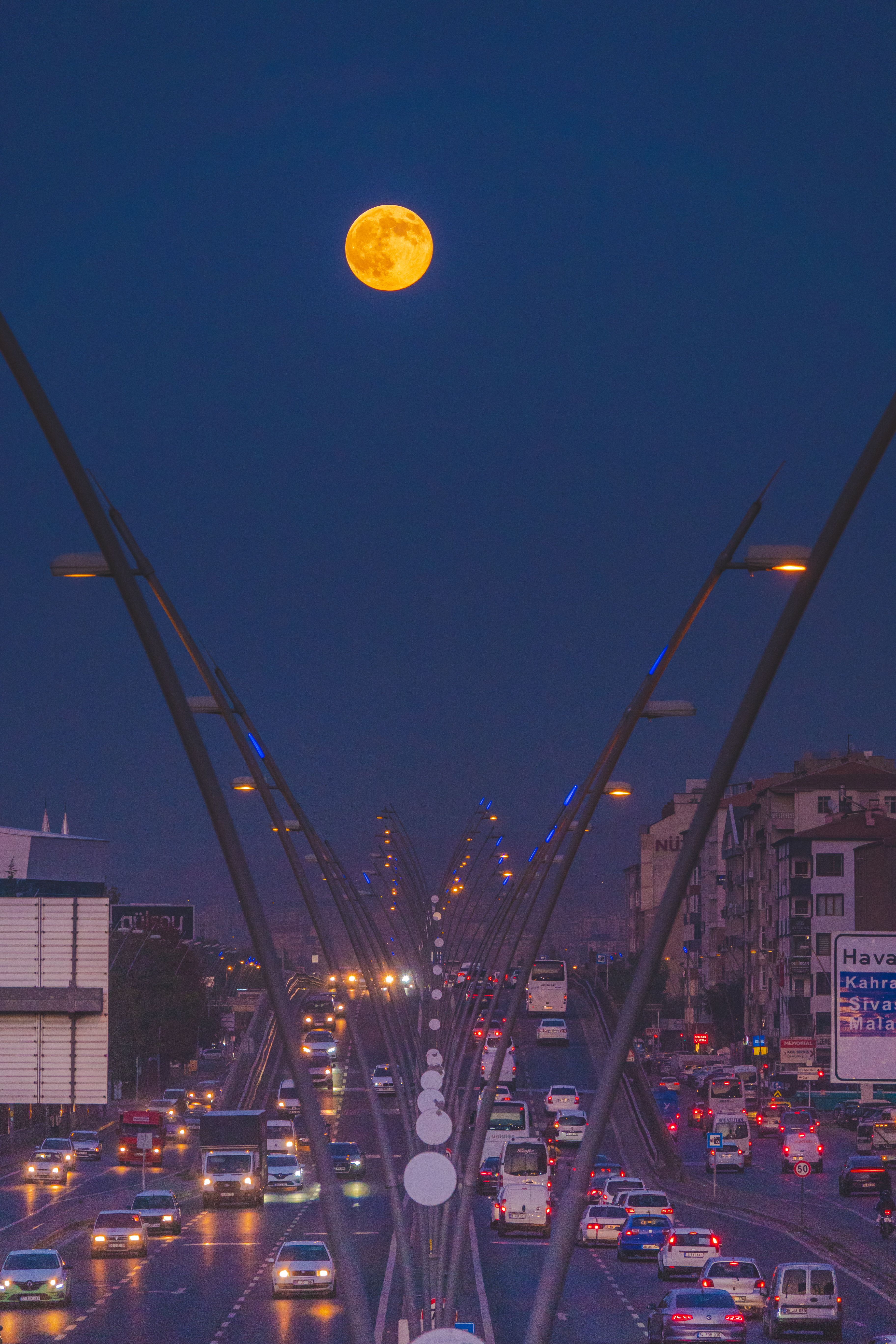 A captivating view of a full moon illuminating a bustling highway in Kayseri during twilight, showcasing urban life.