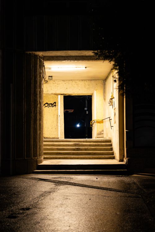 Free A dimly lit urban passageway with moody tones and wet pavement at night. Stock Photo
