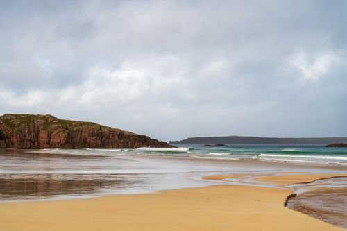 Free Tranquil beach scene with rocky cliffs and gentle waves at Durness, Scotland. Stock Photo