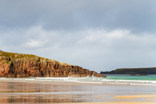 Free Scenic coastal view with rugged cliffs and calm ocean waves on a cloudy day. Stock Photo