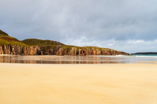 Free Beautiful coastal landscape featuring rocky cliffs and a sandy beach under overcast skies. Stock Photo