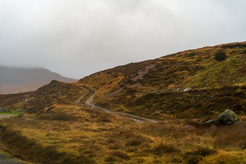 Free Serene landscape featuring a winding path through rolling autumn hills under a cloudy sky. Stock Photo