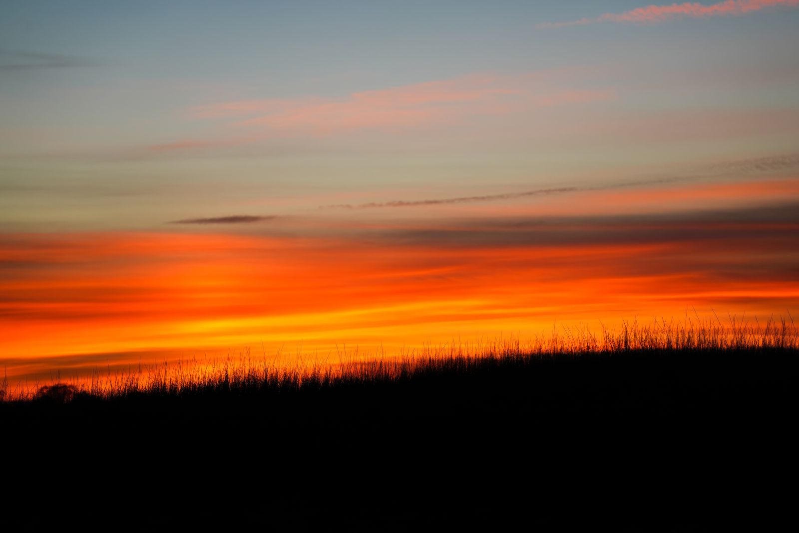 Fiery orange and red sunset behind a silhouetted ridge, photo by Cara Denison on Pexels