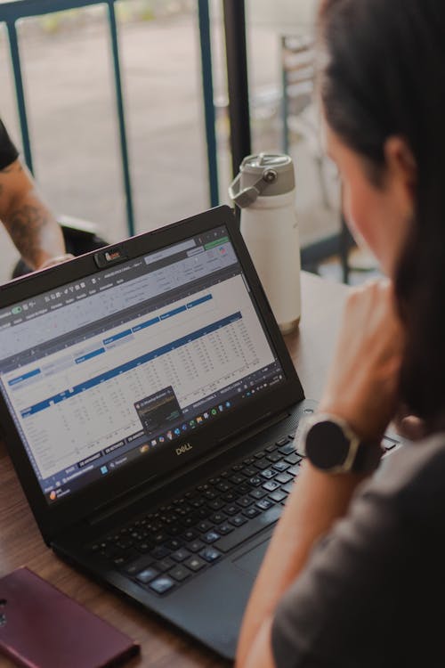 Free Close-up of a person reviewing a spreadsheet on a laptop in a cafe setting. Stock Photo Free Close-up of a person reviewing a spreadsheet on a laptop in a cafe setting. Stock Photo