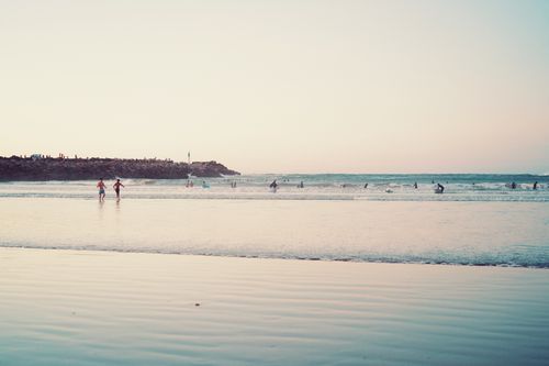 Free A serene beach scene at sunset with people enjoying the calm waves and sandy shore. Stock Photo