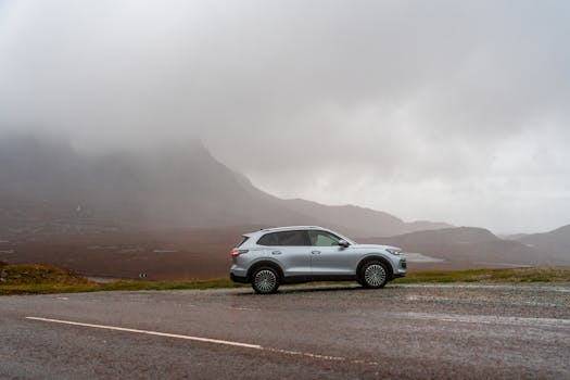 A silver SUV parked on a wet mountain road under cloudy skies, creating a serene and dramatic landscape.